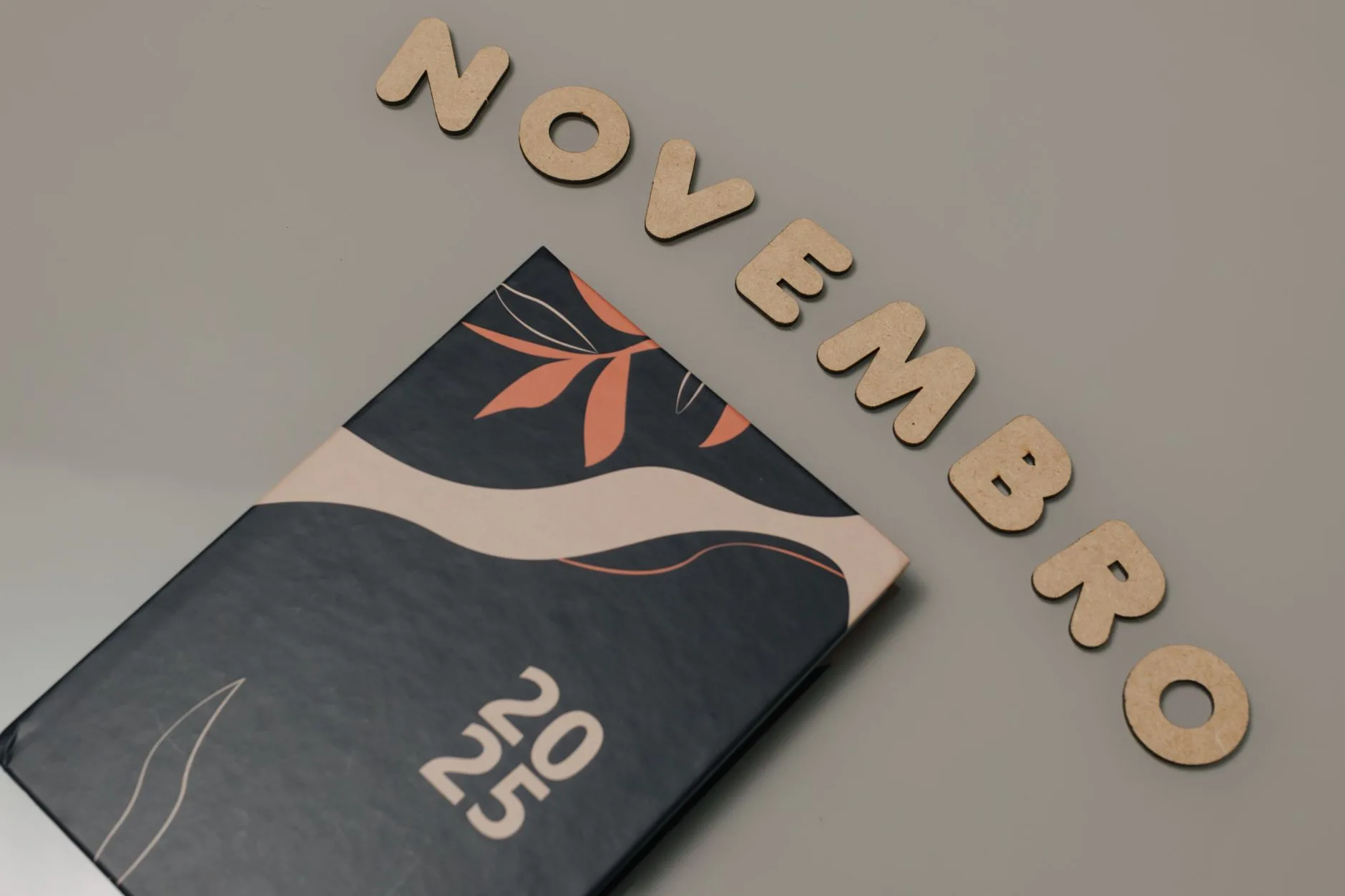 Como criar um novo hábito — Agenda moderna para 2025 ao lado da decoração 'Novembro' em um fundo cinza suave.