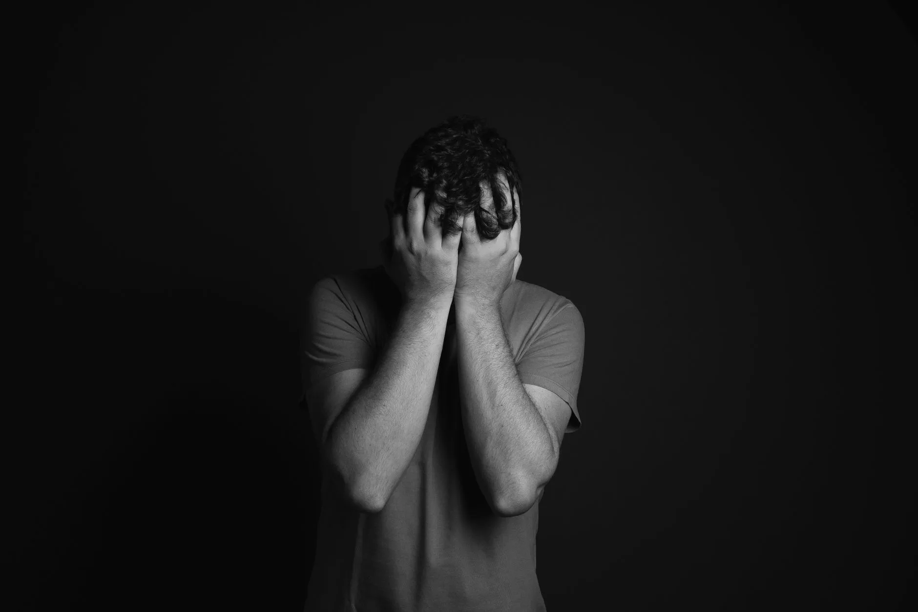 Como lidar com a tristeza sem se cobrar tanto — Um retrato em escala de cinza de um homem cobrindo o rosto, retratando e