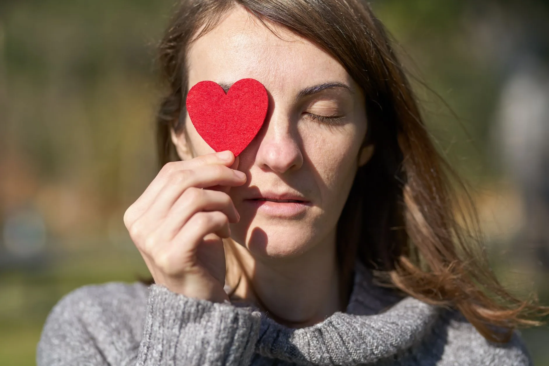 Como validar os próprios sentimentos no dia a dia — Mulher segurando um símbolo de coração vermelho diante de seu olho,